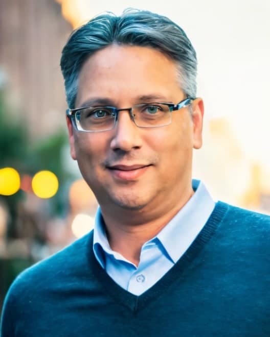 John Castillo, wearing glasses and a blue sweater, on a city street